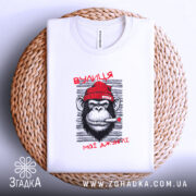 Футболка вулиця мої джунглі, біла, складена на плетеній основі, з принтом мавпи в червоній шапці, що курить, на фоні світло-сірого кольору.