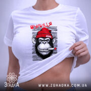 Футболка вулиця мої джунглі, біла, з принтом мавпи в червоній шапці, що курить, на фоні світло-сірого кольору, складена на поверхні, з етикеткою.