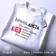 Футболка винна дієта, біла, складена на поверхні, з текстом на передній частині, фон світло-сірий, принт чорний з червоним акцентом на слові 'БЕЗ', етикетка на комірці.