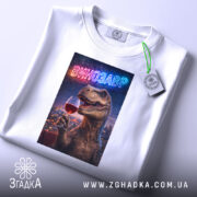 Футболка винозавр, біла, на плоскій поверхні, ракурс зверху, фон світлий, принт з динозавром, що тримає келих червоного вина, з неоновим написом 'ВИНОЗАВР', на етикетці зелена стрічка.