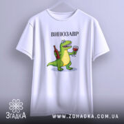 Футболка Винозавр, біла, підвішена на вішалці, фон світло-сірий, принт з зеленим динозавром, який тримає пляшку вина та келих, текст 'ВИНОЗАВР' над принтом.