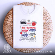 Футболка випускник білого кольору, зображена в плоскому вигляді на плетеній основі. Принт на футболці містить текст 'ВИПУСКНИК' та інші елементи, виконані в червоному, чорному та синьому кольорах. Фон нейтральний, що додає елегантності.