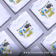 Футболка випускнику 4 класу, біла, на моделі, з легким усмішкою, фон світло-фіолетовий, принт з написом 'Я вижив після 4 років НУШ', з ілюстраціями повітряних кульок і шапки випускника, яскраві кольори, святковий настрій.