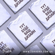 Футболка з вашим дизайном, білого кольору, зображена на моделі в ракурсі спереду, фон світло-фіолетовий, принт чорного кольору з текстом 'ТУТ БУДЕ ВАШ ДИЗАЙН'.