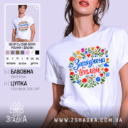 Футболка заряджена теплом, біла, на моделі, з кольоровим принтом, що містить квіти та напис 'Заряджена теплом', фон світло-фіолетовий, деталі принта яскраві та різноманітні.