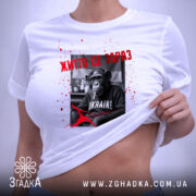 Футболка Життя це зараз, біла футболка, зображена зверху, фон світло-фіолетовий, принт з чорно-білим шимпанзе, текстом червоного кольору та плямами червоного кольору, на ярлику зелена стрічка.