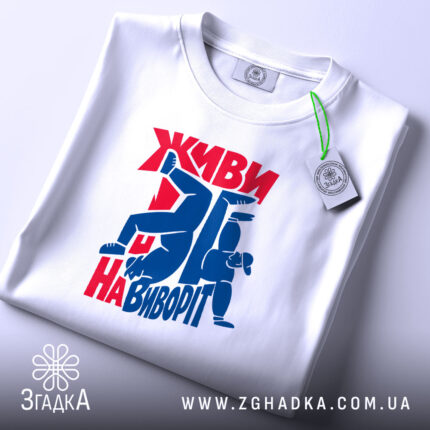 Футболка Живи навиворіт, біла, на столі, з принтом червоного та синього кольору, фон світло-сірий, принт з написом та фігурами людей у динамічних позах, з етикеткою на шнурку.