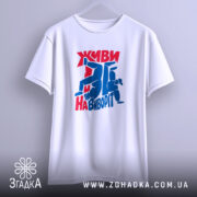 Футболка Живи навиворіт, біла, підвішена на вішалці, з принтом червоного та синього кольору, фон світло-сірий, принт з написом та фігурами людей у динамічних позах.