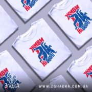 Футболка Живи навиворіт, біла, на моделі, з принтом червоного та синього кольору, фон світло-сірий, принт з написом та фігурами людей у динамічних позах.