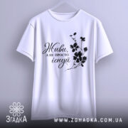 Футболка живи не існуй, біла, зображена з фронтального ракурсу, на фоні світло-сірого кольору, з чорним принтом, що містить напис 'Живи, а не просто існуй' та квітковий візерунок, підвішена на вішалці.