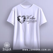 Футболка живи сьогодні, біла, підвішена на вішалці, ракурс спереду, фон світло-фіолетовий, принт чорного кольору з написом 'Живи сьогодні' у формі серця з квітами.