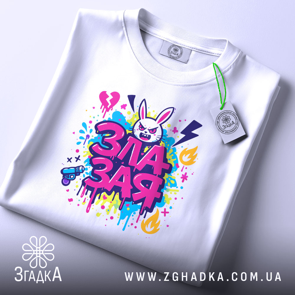 Футболка зла зая, білого кольору, розкладена на поверхні, фон світло-сірий, принт яскравий, з зображенням злого зайця та кольоровими сплесками фарби, етикетка з зеленим шнурком.