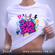 Футболка зла зая, білого кольору, розкладена на поверхні, фон світло-сірий, принт яскравий, з зображенням злого зайця та кольоровими сплесками фарби, етикетка з зеленим шнурком.