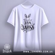 Футболка зла зайка, біла, підвішена на вішалці, фон світло-сірий, принт з зображенням злого зайця та написом 'ЗЛА ЗАЙКА' у чорному кольорі, вид спереду.