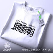 Футболка зроблено з любов’ю, біла, на столі, з чорним принтом у вигляді штрих-коду та написом 'зроблено з любов’ю', на комірці є етикетка, фон світло-сірий.