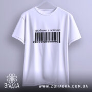 Футболка зроблено з любов’ю, біла, підвішена на вішалці, з чорним принтом у вигляді штрих-коду та написом 'зроблено з любов’ю', фон світло-сірий.