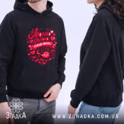 Худі Люблю коли злиш чорного кольору, з капюшоном, на фоні світлого, на моделі, з принтом у червоних тонах, що містить напис "Люблю сильно, сплю мало" та сердечка, з кишенею-"кенгуру" спереду.