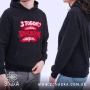 Худі на день закоханих, темно-синього кольору, з капюшоном, на якому зображено пару людей, що носять худі. Принт червоного кольору на грудях з написом "З тобою навіть понеділок норм.". Видно кишеню-«кенгуру», фон світлий.