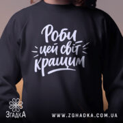 Світшот роби цей світ кращим, чорного кольору, з ракурсу спереду, фон однотонний, принт з написом білим кольором, кругла горловина, манжети на рукавах, фактура гладка та комфортна.