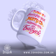 Чашка для майбутньої найкращої бабусі, біла, з яскравим текстом на фронтальній частині, ручка гладка, край рівний, глянцева поверхня, фон світло-фіолетовий, чашка нахилена, створюючи динамічний ефект.