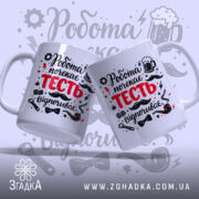 Чашка для найкращого тестя. Дві білосніжні чашки, що стоять поруч, з принтом 'Робота почекає ТЕСТЬ відпочиває'. Ракурс з боку, фон світло-сірий з графічними елементами. Ручки чашок стандартні, краї рівні, поверхня глянцева.