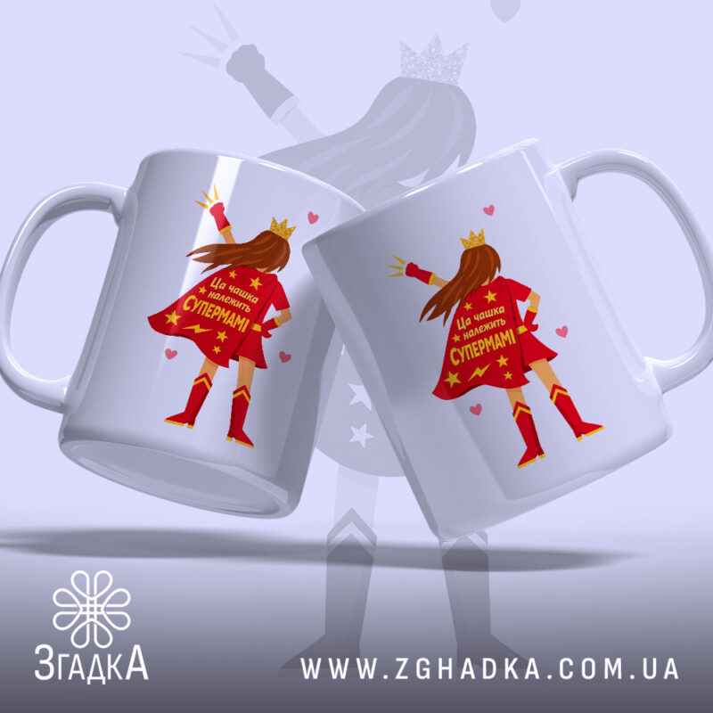 Чашка для Супермами, дві чашки, обидві білі, зображені з легким нахилом, на фоні світло-фіолетового кольору, з принтом супергероїні в червоному плащі, на якому написано 'Ця чашка належить Супермамі', ручки класичні, краї рівні, глянцеві.