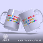 Чашка прикол хочу кавусі. Дві білосніжні чашки з однаковим принтом, на якому написано 'Хочу кавусі, пістолет та на ручці'. Принт яскравий, кольоровий, фон світло-сірий. Ручки чашок гладкі, краї рівні, поверхня глянцева.