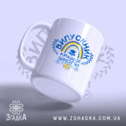 Чашка випускник кращої школи, зображена з легкого ракурсу, на світлому фоні, має яскравий принт з написом 'ВИПУСКНИК КРАЩОЇ ШКОЛИ', ручка круглої форми, край чашки рівний, глянцева поверхня.