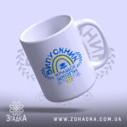 Чашка випускник кращої школи, зображена з легкого ракурсу, на світлому фоні, має яскравий принт з написом 'ВИПУСКНИК КРАЩОЇ ШКОЛИ', ручка круглої форми, край чашки рівний, глянцева поверхня.