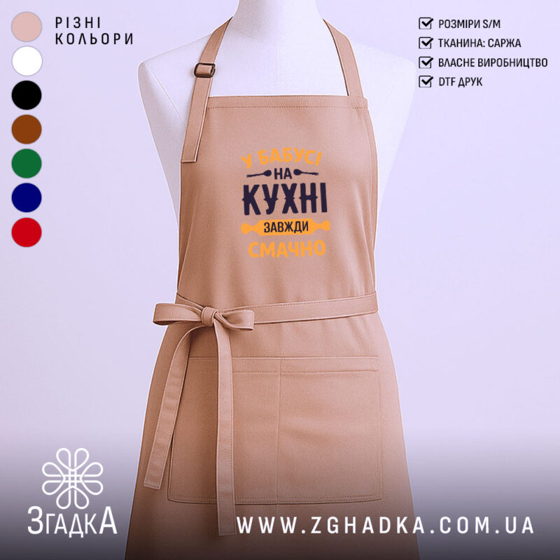 Фартух Бабуся на кухні, бежевого кольору, зображений на манекені з ракурсу спереду, фон світлий, принт з текстом 'У Бабусі на кухні завжди смачно' виконаний в темно-синьому та жовтому кольорах.