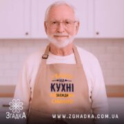 Фартух Бабуся на кухні, бежевого кольору, зображений на дерев'яному фоні, ракурс зверху, принт з текстом 'У Бабусі на кухні завжди смачно' в темно-синьому та жовтому кольорах, поряд з декором у вигляді сніжинки та печива.