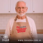 Фартух фестиваль червоних прапорів, бежевий, на літньому чоловікові, кухня на фоні, бренд.