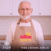 Фартух її величність бабуся, бежевого кольору, зображений зверху на дерев'яному фоні, принт з короною та сердечками, напис червоним і жовтим кольором, поруч з корицею та новорічними прикрасами.