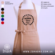 Фартух Мама бежевого кольору, зображений з переднього ракурсу на манекені, фон однотонний світлий, принт чорного кольору з написом 'Мама бренд якості' в оточенні листя.