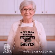 Фартух найкраща бабуся, бежевого кольору, зображений на манекені, фон світлий, принт чорного кольору з текстом 'Ось так виглядає найкраща у світі бабуся'.