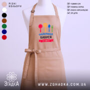 Фартух найкраща бабуся у світі, бежевого кольору, зображений на манекені, фон світлий, принт містить червоний, жовтий, зелений та синій кольори кухонного приладдя.