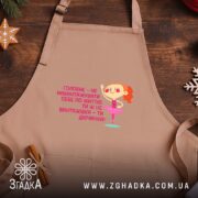 Фартух не навантажуй себе ти ж дівчинка, світло-бежевий, на дерев'яному фоні, бренд.