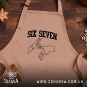 Фартух six seven жест руками, бежевий, на дерев'яному фоні, бренд Згадка.
