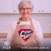 Фартух супер бабуся, бежевий колір, зображений на манекені, фон світлий, принт у формі супергеройського щита з написом 'Супер бабуся' у жовто-синіх кольорах.