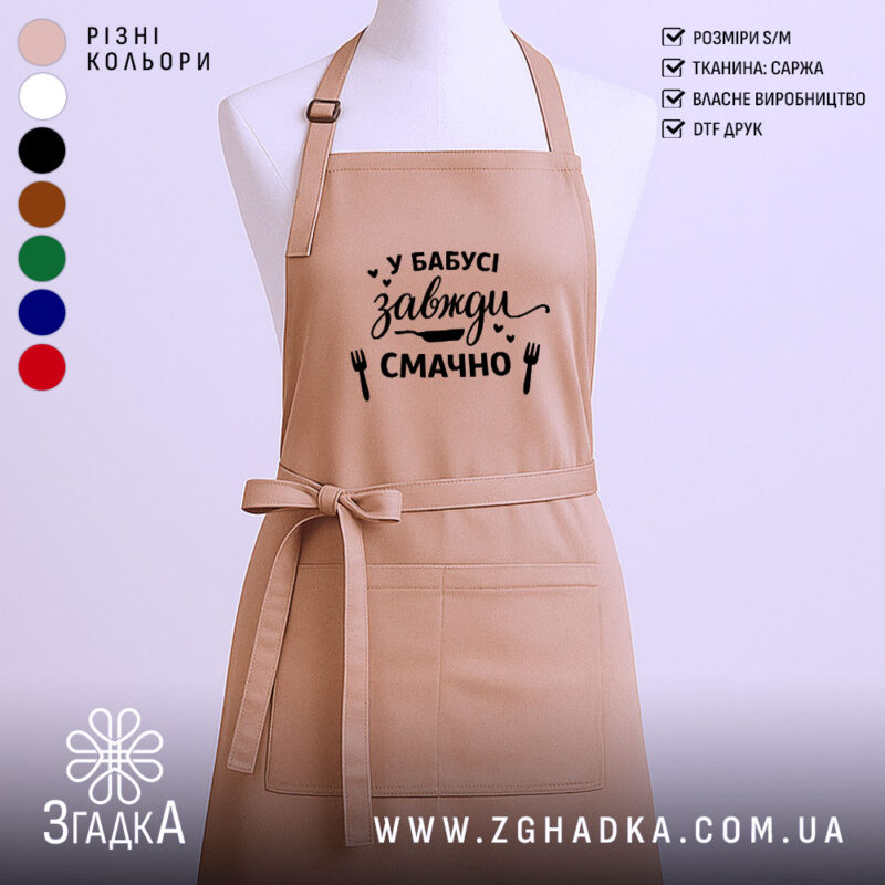 Фартух у бабусі смачно завжди. Фартух бежевого кольору, зображений з фронтального ракурсу на манекені. Фон нейтральний, без зайвих деталей. На фартуху чорний принт з написом 'У бабусі завжди смачно' та малюнками виделки і ножа.
