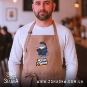 Фартух жени гримні мем дизайн, бежевий, на чоловікові, кафе на фоні, бренд.