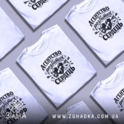 Футболка агентство розбитих сердець білого кольору, зображена на моделі, яка позує в три чверті, фон світло-фіолетовий, принт чорного кольору з малюнком серця, пляшки та конверта.