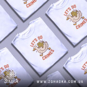 Футболка час для бешкету. Біла футболка на моделі, з принтом, що зображує качку з жабою, яка тримає ніж. Фон світло-фіолетовий, модель позує в три чверті, демонструючи принт.