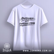 Футболка для серйозних справ. Біла футболка, підвішена на вішалці, фон світло-сірий, принт чорного кольору з текстом 'Футболка для серйозних справ' розташований по центру.