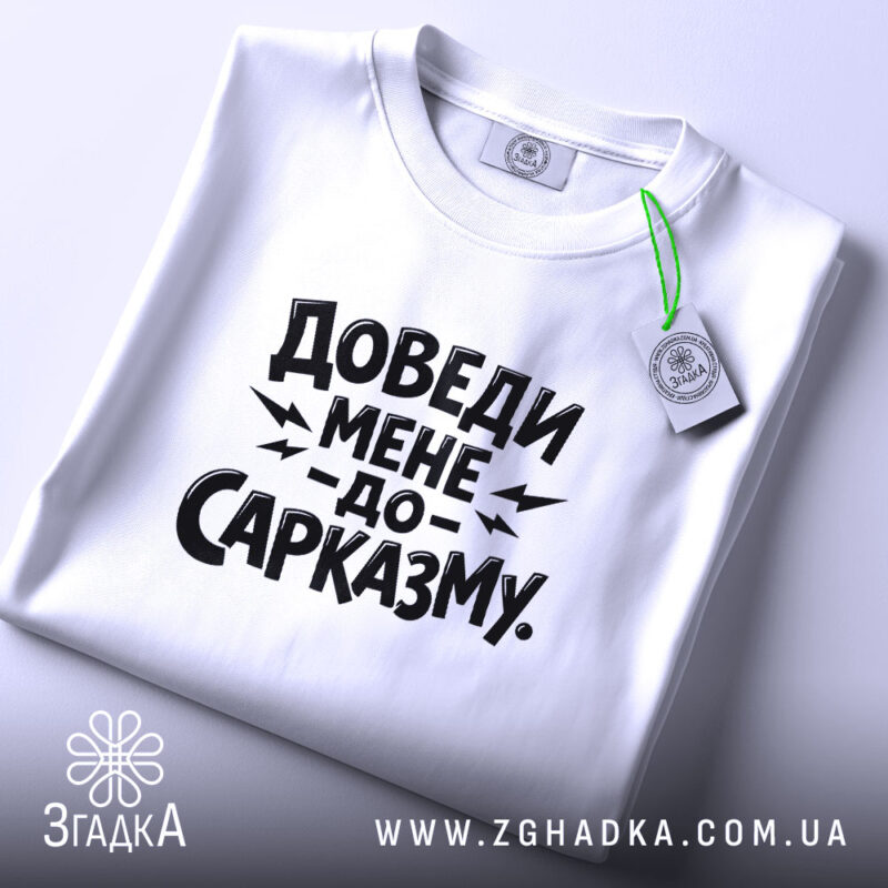 Футболка доведи мене до сарказму, біла, на столі, з етикеткою, фон світлий, принт чорного кольору з великим текстом.