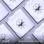 Футболка дух предків, біла, зображена на моделі з легким макіяжем, фон - світло-фіолетовий, принт чорного кольору з птахом та декоративними елементами.