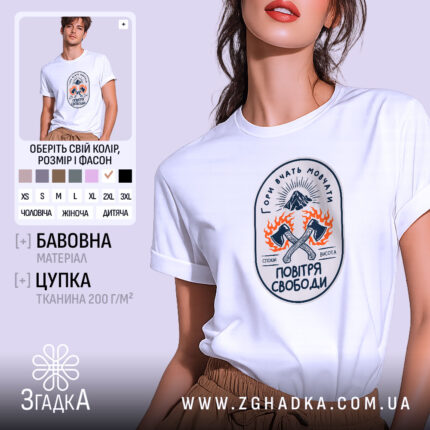 Футболка гори вчать мовчати, біла, зображена на моделі з легким ракурсом, фон світло-фіолетовий, принт з малюнком двох сокир, оточених вогнем, та написом 'Гори вчать мовчати' у верхній частині.