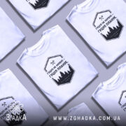 Футболка гуцул не нервує, біла, на моделі, з коротким рукавом, фон світло-фіолетовий, принт чорний з написом "Гуцул не нервує – Гуцул планує" та зображенням лісу.