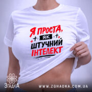 Футболка я як штучний інтелект, біла, зображена в складеному вигляді, фон світло-сірий, принт червоними і чорними літерами з написом 'Я ПРОСТА, ЯК ШТУЧНИЙ ІНТЕЛЕКТ', з етикеткою на зеленій нитці.