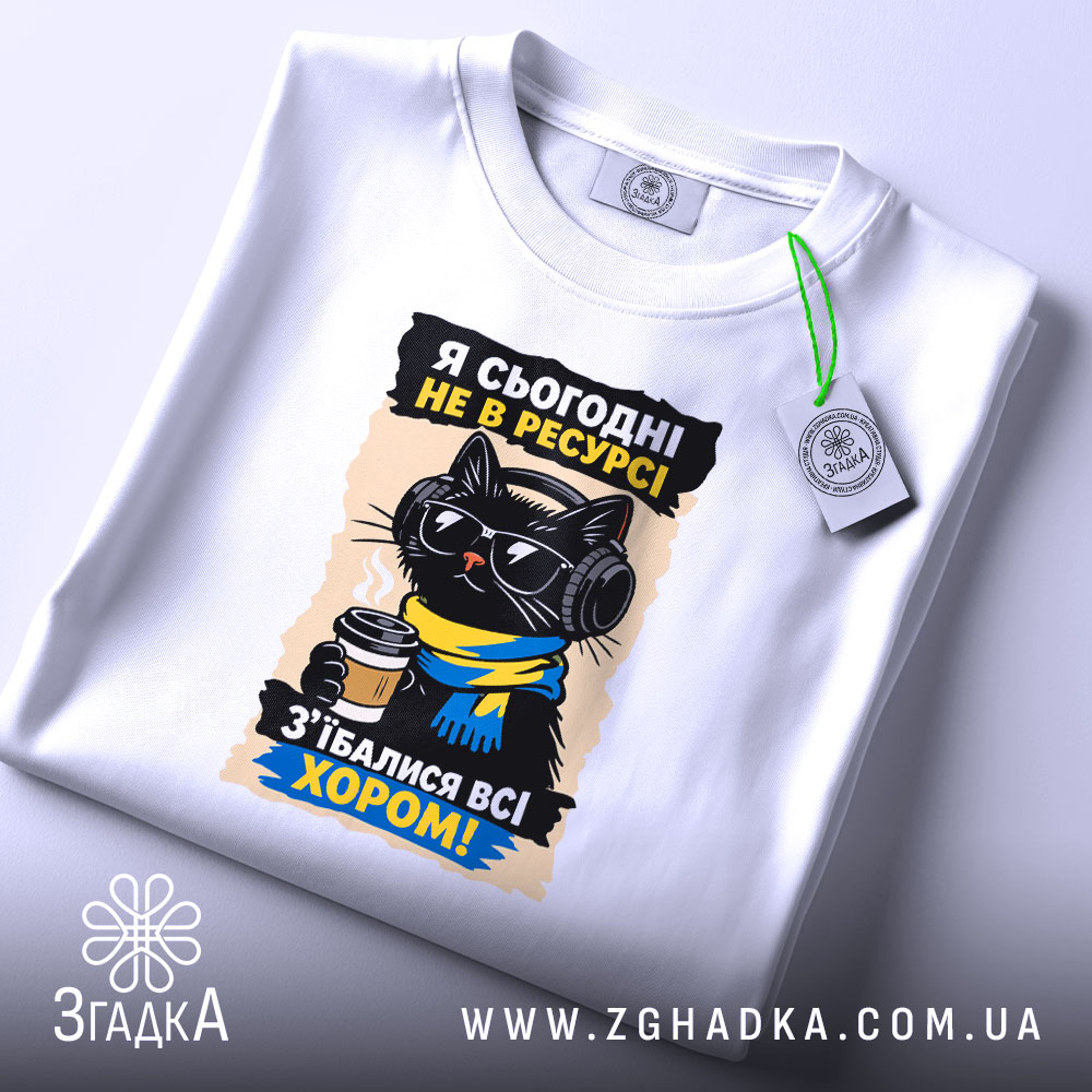 Футболка я сьогодні не в ресурсі. Біла футболка, розкладена на поверхні, з принтом чорного кота в окулярах та навушниках, який тримає чашку кави. Фон світло-фіолетовий, на футболці є етикетка з зеленим шнурком.
